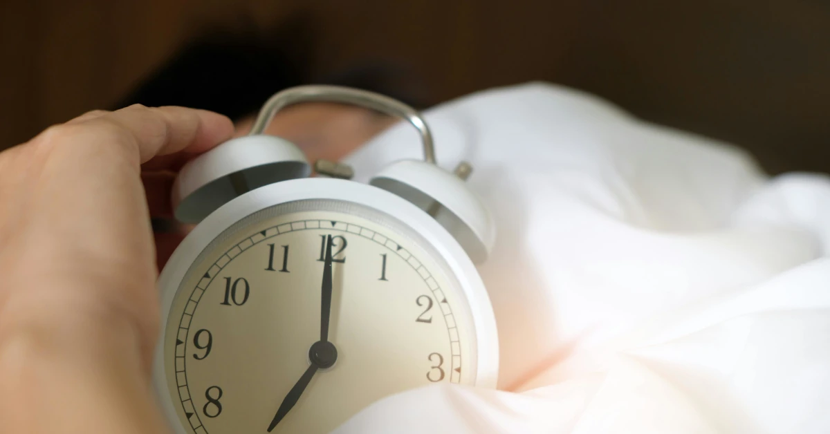 person trying to sleep holding alarm clock